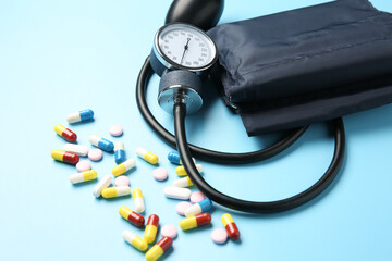 Blood pressure measuring device and pills on light blue background, closeup