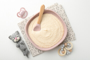 Delicious baby food in bowl with spoon, pacifier and toys on white background, flat lay