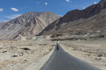Motorcyclist riding on a remote mountain road surrounded by arid landscape