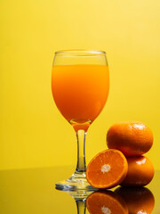 Vertical image of delicious freshly squeezed orange juice in the glass from organic oranges isolated on yellow background with copy space