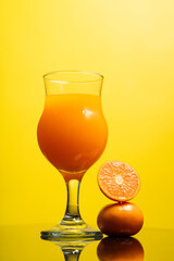 Vertical image of delicious freshly squeezed orange juice in the glass from organic oranges isolated on yellow background with copy space