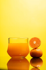Delicious freshly squeezed orange juice in the glass from organic oranges isolated on yellow background with copy space