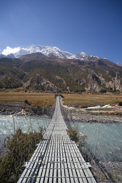 A suspension bridge leading towards a mountain range under a clear blue sky.