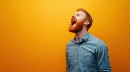 Young man with a red beard in a blue shirt, shouting joyfully against a light orange wall, bright lighting stock minimalist photo
