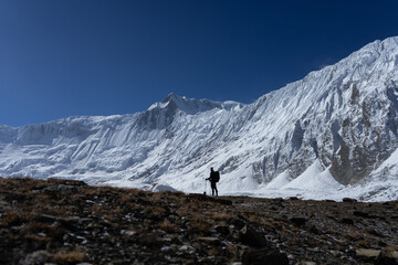 A hiker stands in awe of the majestic, snowy mountain range under a clear blue sky.
