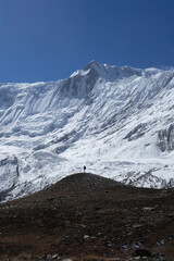 Fototapeta premium A lone hiker stands on a hill, gazing at a majestic snow-covered mountain range under a clear blue sky.