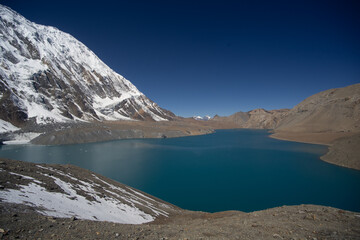 A stunning view of a tranquil mountain lake surrounded by snow-capped peaks under a clear blue sky.