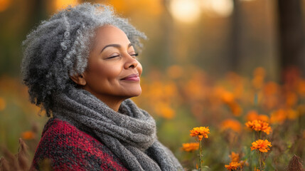 A woman with curly gray hair closes her eyes, savoring the tranquility of a flower-filled forest during autumn