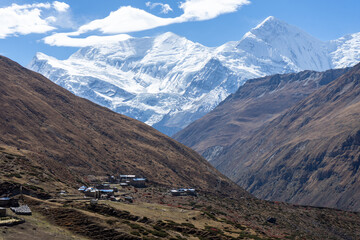 A remote mountain village nestled in a valley, surrounded by towering snowy peaks.