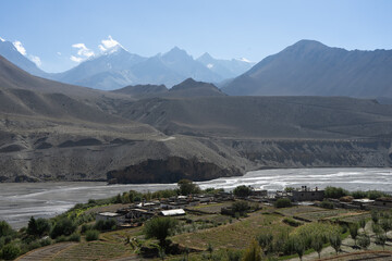 A serene mountain village nestled in a tranquil valley with a river and vast mountainous backdrop.