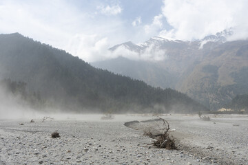 A misty mountain landscape with a riverbed and cloudy skies.