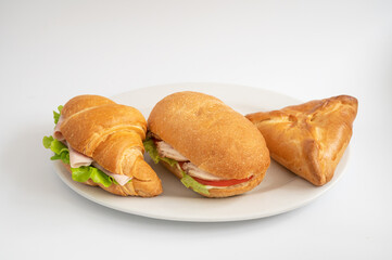 A plate with two croissant sandwiches, one baguette sandwich, and a savory pastry. Ideal for a light lunch or snack.