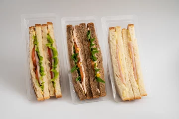 Three packaged sandwiches with white and whole wheat bread, filled with lettuce, tomatoes, turkey, cheese, ham and greens. Ideal for quick meals. © olinchuk