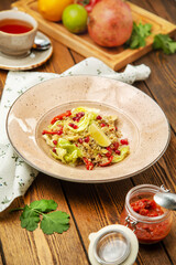 Quinoa salad with pomegranate seeds, cherry tomatoes and lemon in a plate, cafe, restaurant, wooden table. Vertical photo