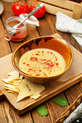 Cheese soup with paprika and corn chips in a plate, cafe, restaurant, on a wooden table. Vertical photo