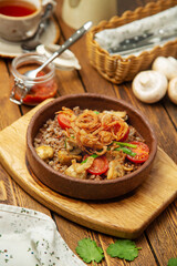 Buckwheat porridge with mushrooms, fried onions and cherry tomatoes in a plate, cafe, restaurant, on a wooden table. Vertical photo