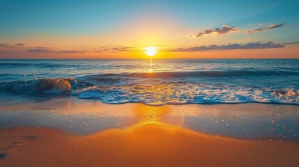 Fototapeta premium Sunset on the beach with warm orange and yellow hues, clear blue sky, gentle waves, and visible footprints in the sand, captured in high-definition photography.
