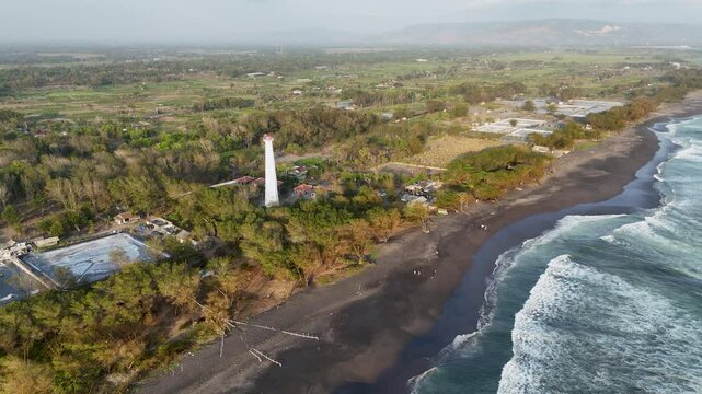 Lighthouse stands tall amidst lush greenery and ocean waves on a tranquil coastline
