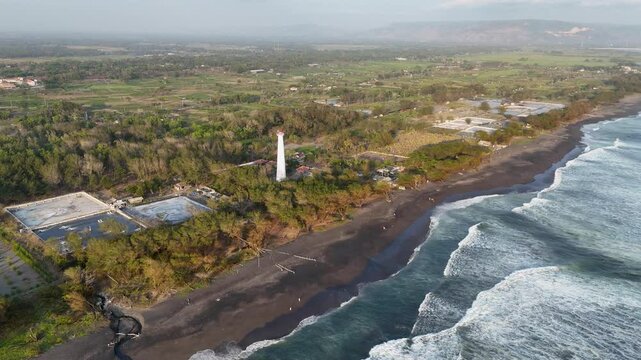 Lighthouse stands tall amidst lush greenery and ocean waves on a tranquil coastline