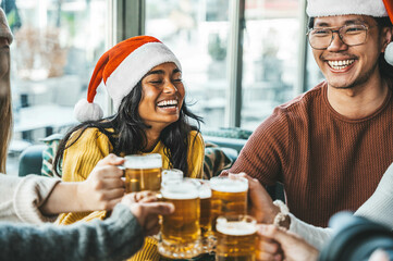 Happy friends wearing santa claus hat toasting beer glasses at brewery pub restaurant - Group of young people enjoying Christmas dinner party together - Winter holidays concept