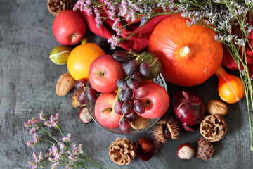 Fototapeta premium Colorful still life with seasonal fruit and vegetables on fark grey textured background with copy space. Close up photo of pumpkin, apples, grape, chestnut, onion and squash. 