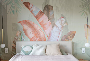 Modern interior of bedroom with comfortable bed with pillows and textured wallpaper od the wall with leaves pattern. Design house and cozy home.