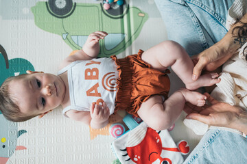 Baby girl lying on her back on a playmat, playing with her mom. Baby girl lying on back, being...