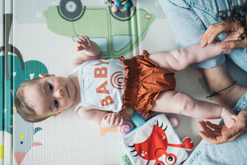 Baby girl lying on her back on a playmat, playing with her mom. Baby girl lying on back, being...