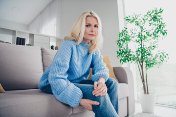 Photo of pretty aged woman sit couch touch hurt knee joint wear pullover free time modern apartment...