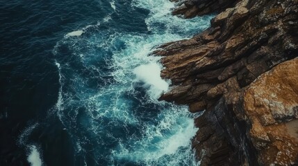 aerial perspective of crashing ocean waves against rugged rocks, the deep blue waters creating a striking contrast against the earthy tones of the shore, exuding a sense of power and tranquility