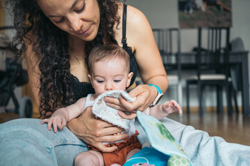 Mother cleaning her baby girl's mouth with a white cloth. Young mother cleaning her baby's mouth...