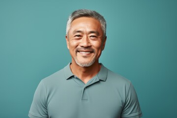 Obraz premium Portrait of a happy asian man in his 60s donning a classy polo shirt isolated on soft teal background