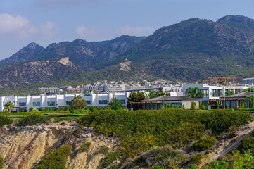 Luxurious hillside residences overlooking the vibrant coastal town beneath majestic mountains on a sunny day