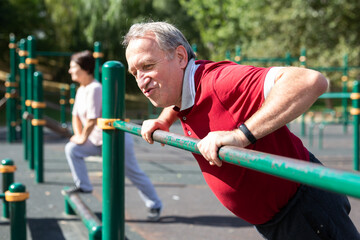 Elderly man doing exercises on a horizontal bar at an outdoor sports ground