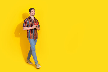 Full length portrait of nice young man phone walk empty space wear shirt isolated on yellow color background