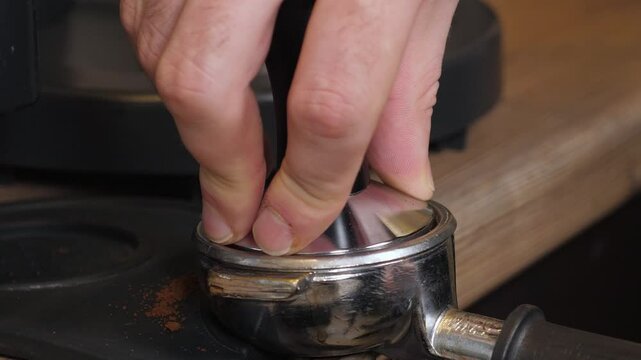Close-up of a barista tempering freshly ground coffee with a tempera in a coffee shop. The process of making espresso.