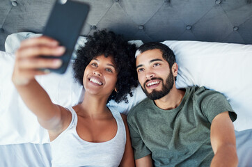 Fototapeta premium Couple, smile and love in bed with selfie to relax, break and memories at home in Brazil. People, relationship and above in bedroom to rest for social media, post or profile picture for bonding