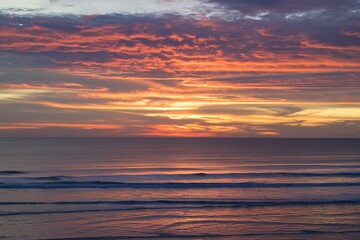 Obraz premium Sunset over the ocean with waves and a dramatic sky