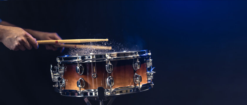Drum sticks hitting snare drum with splashing water on black background.
