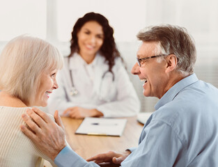Fototapeta premium Heathcare Concept. Back view of happy senior husband comforting his wife during consultation with mexican doctor