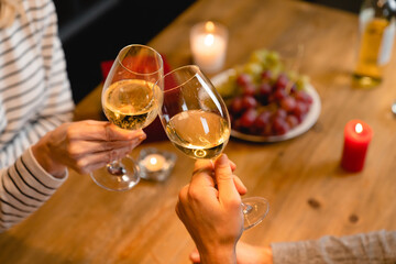 Cropped photo of clinking glasses of wine with romantic dinner in the background. Dining at home, indoors in restaurant. Dating and relationship. Valentine`s Day and anniversary