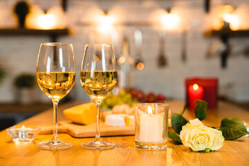 Shot of a romantic dinner table with glasses of wine, candles and rose in the kitchen. Valentin`s day, anniversary, engagement, proposal, romantic atmosphere. No people