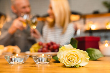 Focused shot of a romantic dinner with candles and a rose and happy couple in the background. Valentine`s day, proposal, engagement, anniversary celebration. She said yes