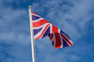 Union Jack flag waving against a blue sky with clouds during a sunny day in the United Kingdom