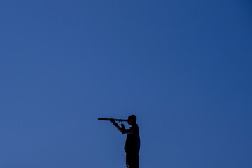 silhouette of man with spyglass, blue sky in the background