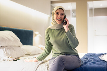 Obraz premium A joyful woman wearing a hijab engaging in a cheerful conversation on her smartphone. The setting conveys comfort and happiness.
