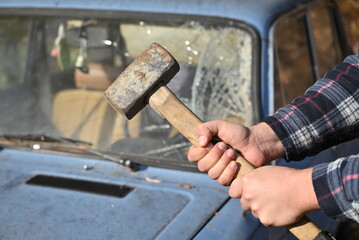 A man is clutching a hammer in front of a bright blue car