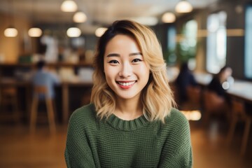 Portrait of a cheerful asian woman in her 20s wearing a cozy sweater isolated on lively classroom background