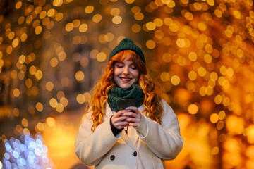 A cheerful ginger woman is texting messages on street on new year's eve.