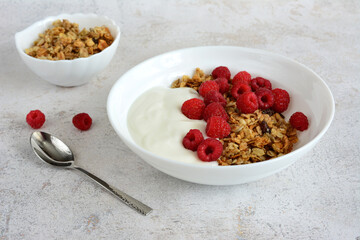 a bowl of cereal with yogurt and a handful of raspberries next to it
